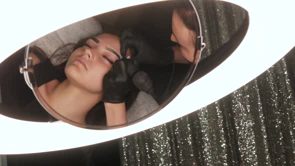 Master Applies Dark Coloring Pigment to Correct Shape of Eyebrows with a Special Machine alt