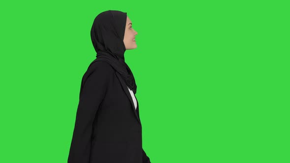 Smiling Islamic Female Model Wearing Hijab Walking and Looking Ahead on a Green Screen, Chroma Key. alt