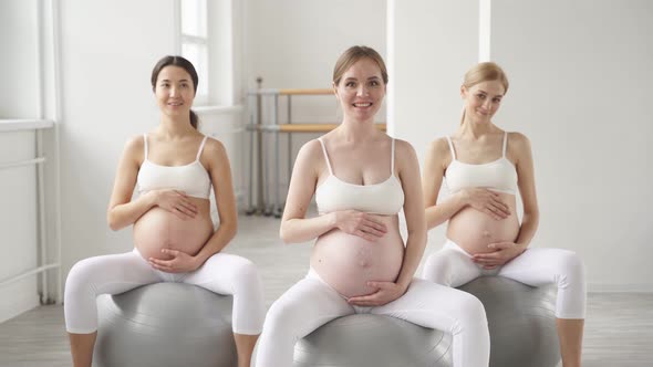 Cute Diverse Pregnant Women with Naked Tummy Sit on Fitballs Engaged in Perinatal Gymnastics