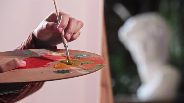 A Young Woman in Art Workshop Putting an Orange and Blue Colors on the Palette alt