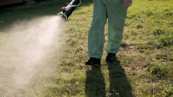 Farmer in Protective Clothes Spray Pesticides. Farm Worker Spray Pesticide Insecticide on Green alt
