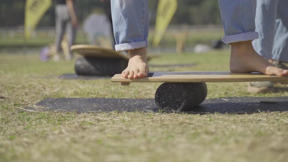 A ground level stationary footage of a balance board exercise with bare feet in an outdoor public pa alt