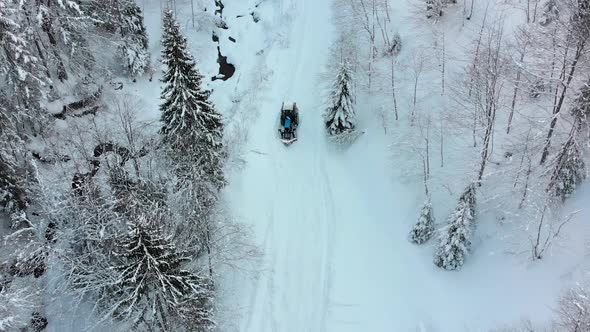 Aerial View on a Lonely Tractor Riding on Path in a Snowy Winter Forest alt