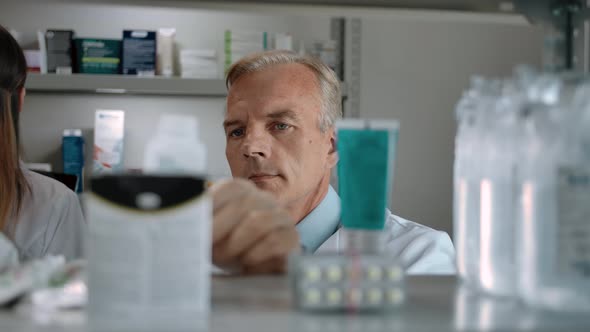 An Adult Man Pharmacist Audits the Product in the Interior of a Modern Pharmacy alt