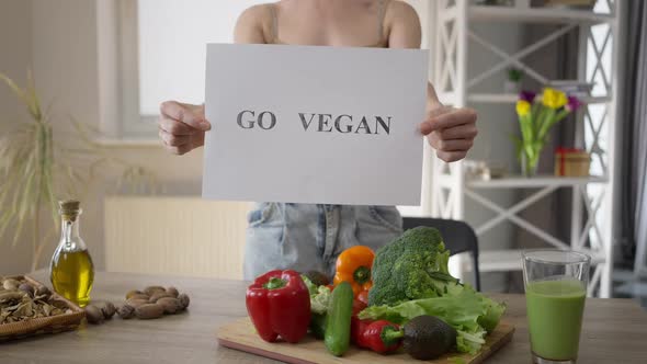 Unrecognizable Woman Showing Go Vegan Standing at Table with Healthful Food alt