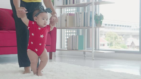 Happy family with mother support baby step walk in the living room at home.