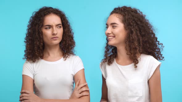 Two Beautiful Young Curly Female Twins Touching Each Other Hair Smiling on Blue Background alt