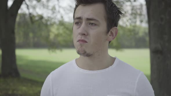Closeup Portrait of Depressed Young Caucasian Man Standing in Summer Park Outdoors alt