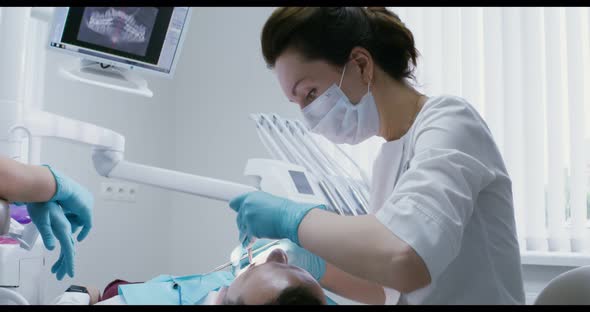 A Female Dentist Examines the Oral Cavity of a Patient Lying on a Dental Chair alt