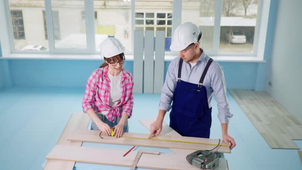 Woman and Man Builtin Hard Hats Measure Laminate with Tape Measure for Renovating Floor in New alt