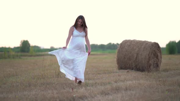 Beautiful Pregnant Woman in Wheat Field with Haystacks at Summer Day alt