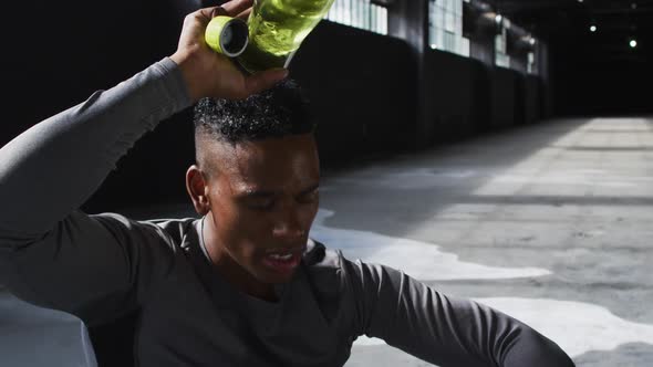 African american man sitting in an empty building pouring water on his head alt