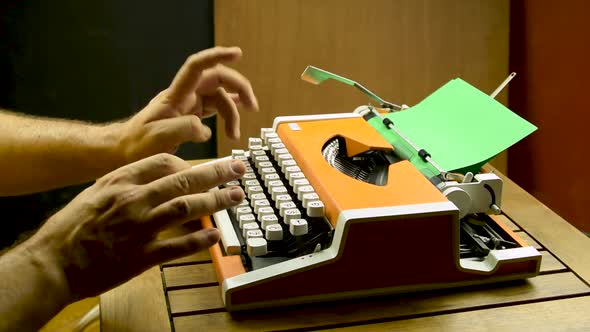Male hands typing on a typewriter. Orange vintage mechanical old. Green paper.