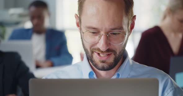 Portrait of Smiling Businessman Sitting at Desk with Laptop in Modern Open Plan Office alt