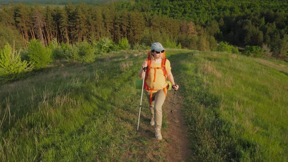 Young Woman Traveler with Backpack and Trekking Poles Climbing the Mountain alt