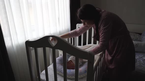 Mom Straighten the Blanket at the Sleeping in the Crib of the Newborn alt