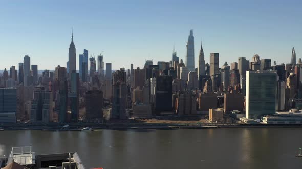 A high angle, aerial view over a calm East River on a sunny day with blue skies. The drone camera fa alt