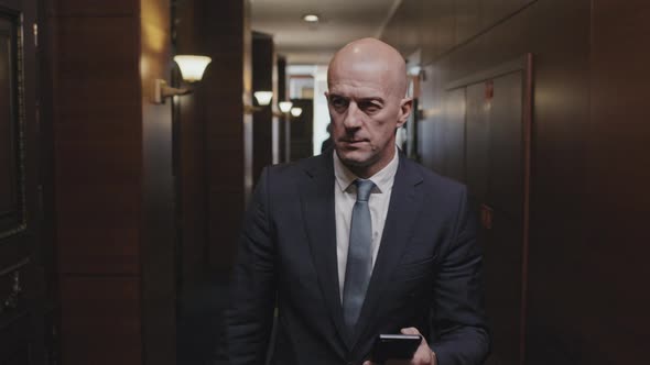Businessman Walking with Phone in Corridor of Office Center alt