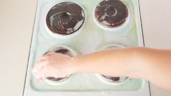 A Hand Rubs the Surface of a White Electric Stove with a Foam of Detergent with a Sponge alt