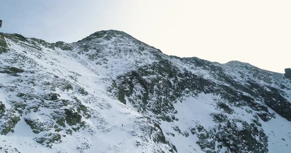 Backward Aerial Over Winter Snowy Mountain with Mountaineering Skier People Walking Up Climbing