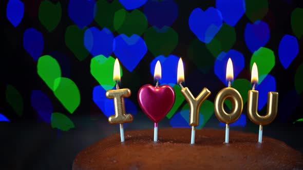 Pan Shot of Simple Valentines Day Cake with Lit i Love you Candles with a Colorful Background