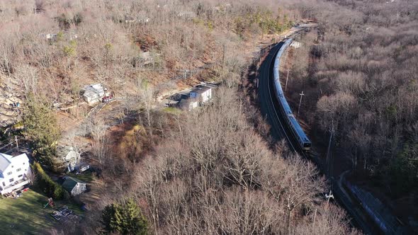 And aerial view over a train leaving the station on a sunny day. There are brown, leafless trees all alt
