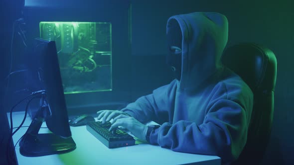 Cybercriminal Hacker Typing and Looking at the Clock on His Hand alt