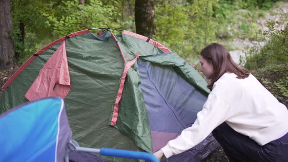 A Young Female Tourist Opens a Green Tent Set Up in the Forest