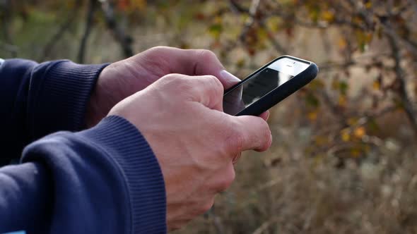 A man is sitting with a phone in his hands. Closeup man in nature writes a message alt