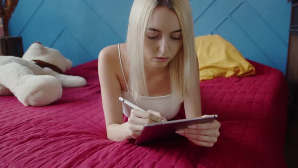 Young Woman Artist Draws Lying Bed on Graphic Tablet Using Stylus Front View alt