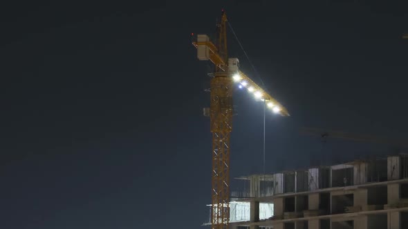 Building Construction at Night. Timelapse. Tower Crane on a Construction Site with Lighting alt