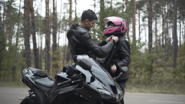 Smiling Loving Middle Eastern Biker Fastening Girlfriend's Pink Helmet Outdoors. Handsome Boyfriend alt