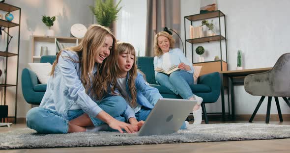 Woman Reading Book on the Couch while Her Active Friendly Eldest and Younger Daughters Playing alt