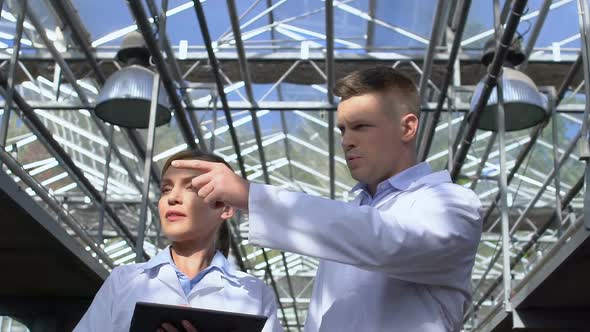 Man and Lady in White Suits Walking in Greenhouse, Analyzing Experiment Results