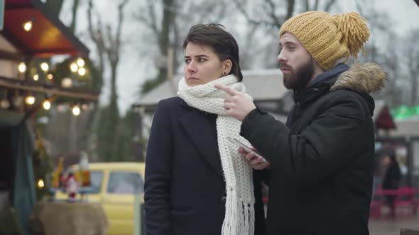 Young Bearded Caucasian Man in Yellow Hat Using Smartphone As His Girlfriend or Wife Talking with alt