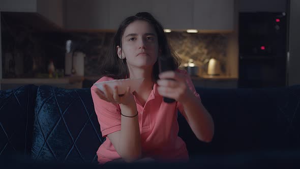 Teenage Girl Eating Chips Out of a Large Bowl Watching TV and Changing Channels Sitting at Home alt