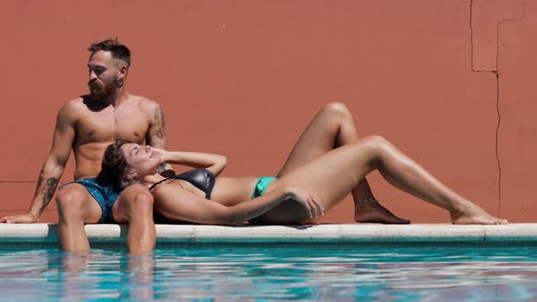 Couple in swimwear resting on poolside alt