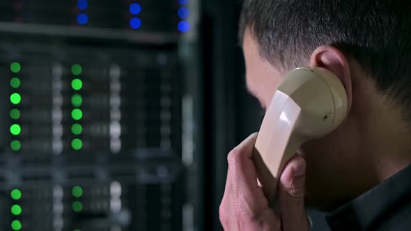 A man calls on an old phone against the backdrop of a modern server cabinet alt