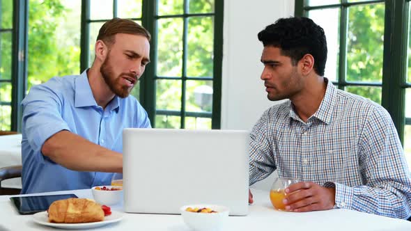 Male executives toasting juice glasses while working on laptop 4k alt