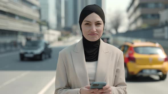 Portrait of Successful Business Woman Standing with Smartphone and Smiling on Camera alt