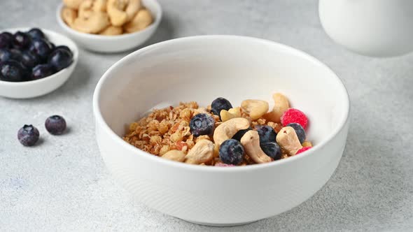 Pouring milk in granola on white background. Granola with nuts and berries. Healthy breakfast.