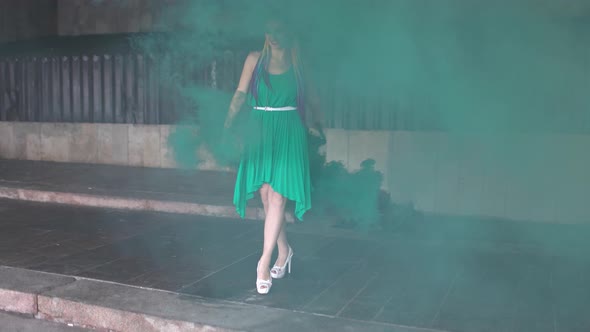 Cute Girl in a Green Dress with African Braids and Colorful Makeup Posing with Bright Green Smoke on alt
