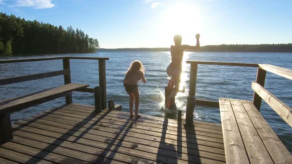 Family Couple with Daughter Running on a Wooden Pier and Jumping Into the Lake alt
