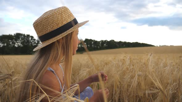 Thoughtful Little Girl in Straw Hat Sitting in the Wheat Field and Touching Spikelet. Beautiful alt