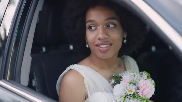 Closeup Portrait of Romantic Happy Bride with Wedding Bouquet Sitting in Car Smiling alt