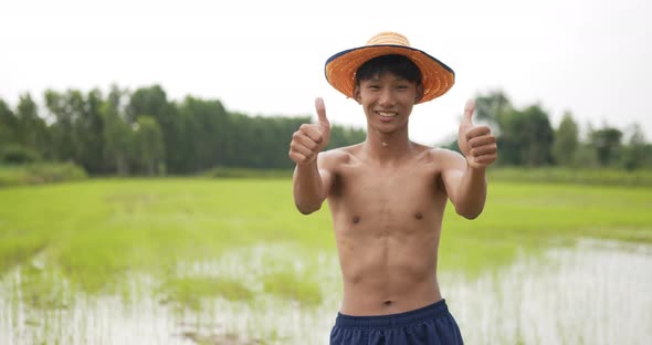 Young farmer topless standing and arms folded in rice field alt