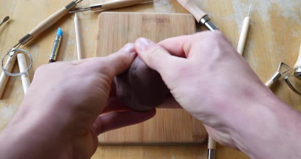 Close up on the hands of an artist or sculptor making a figurine out of brown modeling clay in his a alt