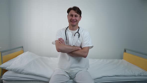 Portrait of Confident Doctor Crossing Hands Looking at Camera Smiling Sitting on Bed in Comfortable alt