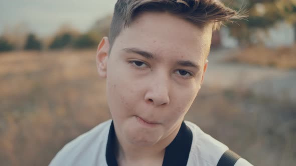 Portrait of Suspicious Sly Pimply Teen Boy Chews Looking Into the Camera alt