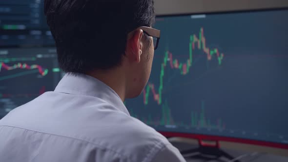 Asian Male Stock Market Broker Looking Analyzing Graphs On Multiple Computer Screens alt